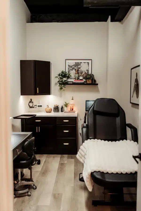 IPL Photofacial in Waunakee, WI 3 Treatment room at Loure Aesthetics with a black reclining treatment chair, rolling stool and dark wood counter with cabinets