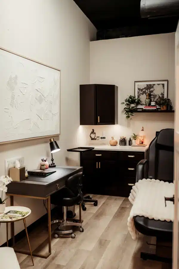 IPL Photofacial in Waunakee, WI 2 Treatment room at Loure Aesthetics with a dark wood desk, office chair and black leather treatment chair with a white blanket